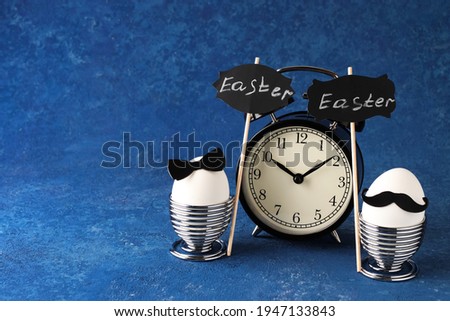 Easter creative holiday concept. White eggs of a chicken farm on a blue background. Couple with black bow and mustache for breakfast. Alarm clock and time. Copy space.