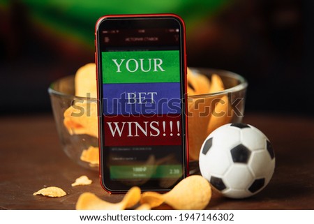 Mobile app for online betting and potato chips. Football match online broadcast on laptop screen on the background