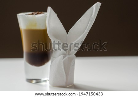 Coffee drink shot with a nutty note with fluffy milk foam, decorated with chocolate shavings, served with an Easter bunny-shaped napkin, sweet drink