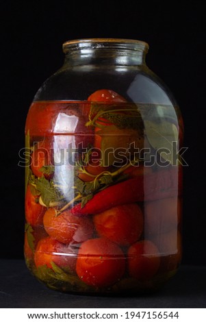 Pickled tomatoes on a black background. Pickled tomatoes in a container on a dark background. Canned vegetables