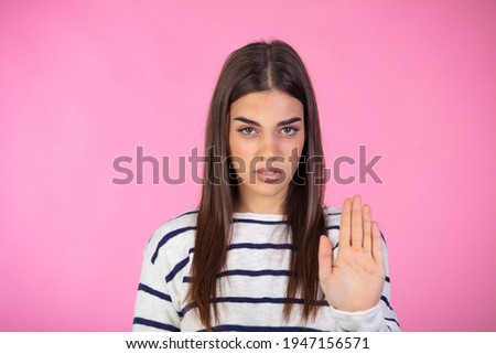 Woman making stop gesture with her hand. Prohibition symbol. Closeup portrait of young, serious, pretty, charming girl in sweater making stop gesture with palm of her hand on pink background