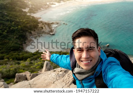 Young smiling man take a selfie photo of beautiful seascape panorama of Porto Giunco beach in Sardinia, Italy