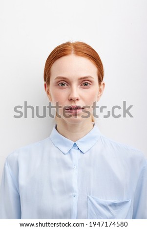 Confident female with natural red hair in blue blouse posing at studio wall, having calm expression