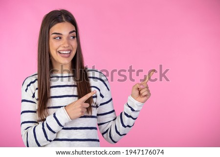 Expressive trendy girl with long brown hair wearing sweater and showing away on pink backdrop. Cute young woman with a bright idea or solution pointing up with her finger while laughing 