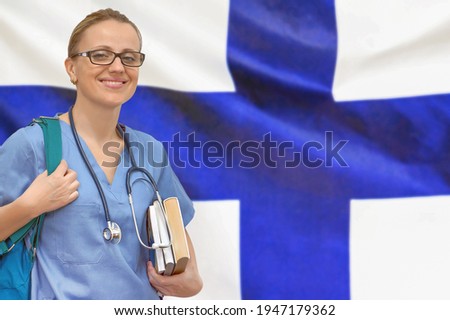Female student doctor with stethoscope and books in hand on the Finland flag background. Medical education concept. Medical learning in Finland