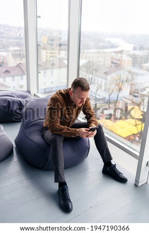 Young successful male businessman is sitting near a large window in the office and relaxing. Rest after a working day