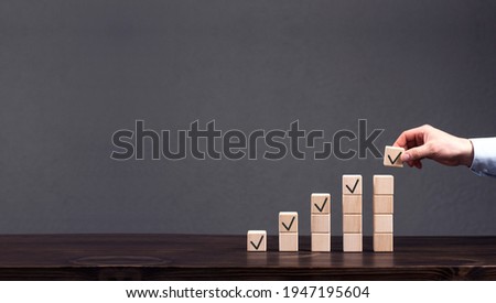 Wooden cubes are stacked in ascending order. The businessman's hand puts the top cube. Profit, finance growth concept. Progress Royalty-Free Stock Photo #1947195604