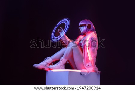 Beautiful woman with purple hair in futuristic costume over dark background. Girl in glasses of virtual reality. Augmented reality game, future technology, AI concept. VR. Neon light. Royalty-Free Stock Photo #1947200914