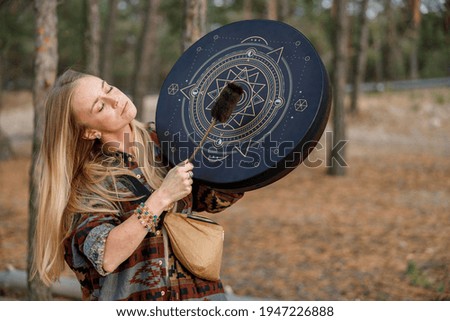 Young ethnic mature shaman female is walking and playing drums meditative music