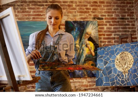 Young beautiful female artist painting on canvas using oil paintings and palette knife. Painter creating artwork in art studio. Relaxation, leisure, hobby, stress management
