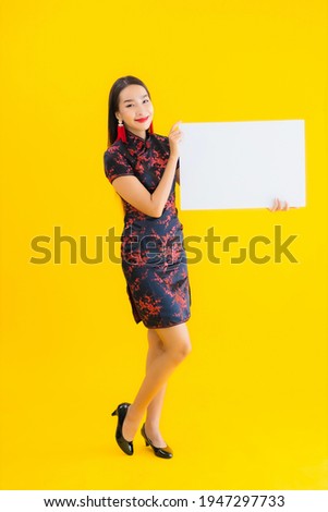 Portrait beautiful young asian woman wear chinese dress show white empty billboard for text in chinese new year concept on yellow isolated background