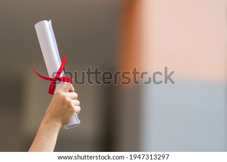 Close-up shot of a university graduate holding a degree certification to shows and celebrate education success on the college commencement day with sunlight in the background. Royalty-Free Stock Photo #1947313297
