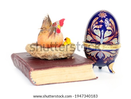 a porcelain Easter egg and an old religious book with a decorative chicken lying on it
