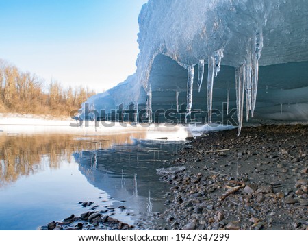 Icicles hang under the ice against the background of a fallen river in spring Royalty-Free Stock Photo #1947347299