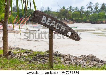 Wooden sign Beach on tropical coast. Low tide landscape with signpost Beach. Beach with palm trees and boats. Paradise direction. Tropical island seascape. Summer vacations. Travel destinations. 