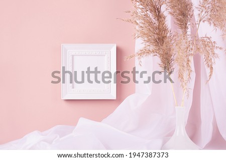 Elegant home decoration - square blank photo frame hanging on pink wall, curtain, beige fluffy reeds in vase. Contemporary simple life style.