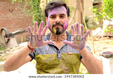 the young man paint on the face with hand over out of the focus green brown background.