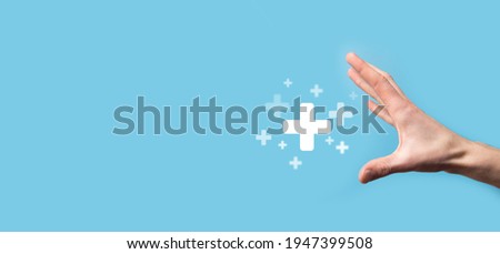 Male hand holding plus icon on blue background. Plus sign virtual means to offer positive thing like benefits, personal development, social network Profit,health insurance, growth concepts. Royalty-Free Stock Photo #1947399508