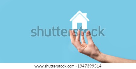 Male hand holding house icon on blue background. Property insurance and security concept.Real estate concept