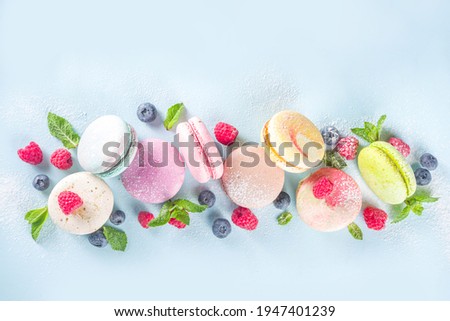 Colorful french macaron dessert. Set of various different tastes and color macaron cookies with berries, sugar powder and mint on blue background
