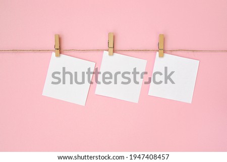 Empty paper sheet for notes, frames that hang on rope with clothespin and isolated on pink background. White blank with empty space for text.