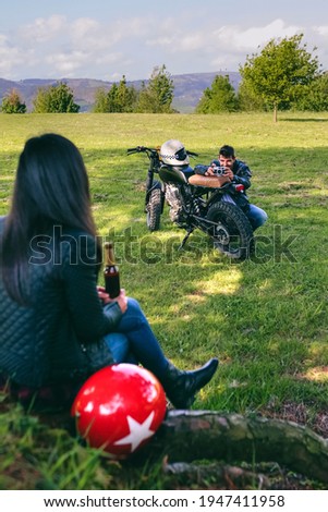 Young couple resting from a motorcycle trip taking picture outdoors. Selective focus on man in the background