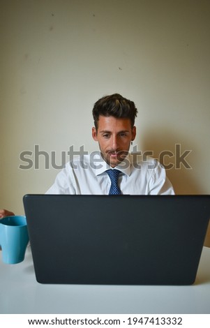 A bearded caucasian businessman working from home with a mug next to his laptop