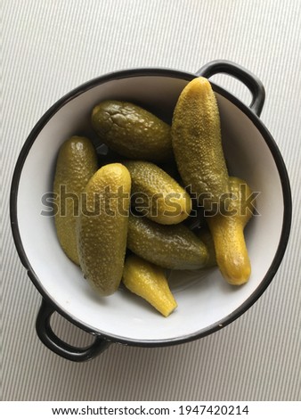 pickled cucumbers close-up lie in a bowl with black edges on a gray striped background