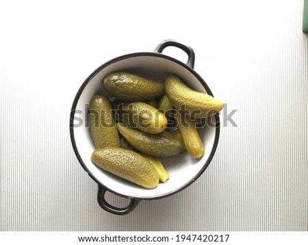 pickled cucumbers close-up lie in a bowl with black edges on a gray striped background