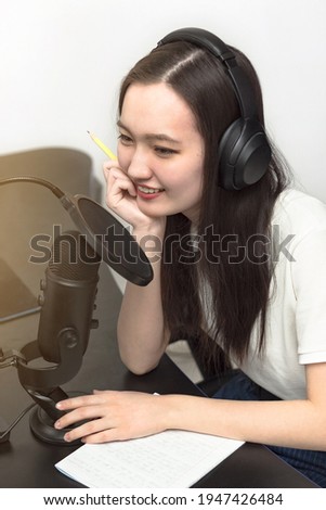 Young smiling woman with professional microphone and headphones recording podcast at studio, technology and media