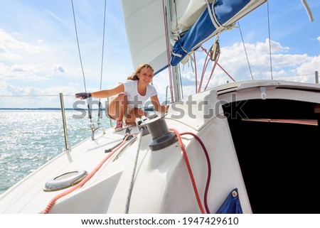 Young woman sailing on a yacht. Female sailboat crewmember trimming main sail during sail on vacation in summer season Royalty-Free Stock Photo #1947429610