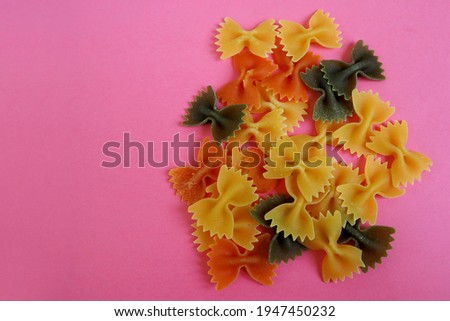 close up a lot of raw farfalle tricolors lie on a pink background top view . italian cuisine