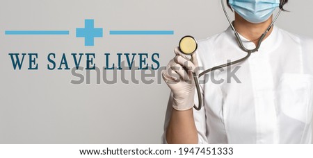 We save lives - concept of text on gray background. Nearby is a cropped view of doctor in white coat, protective face mask and stethoscope. Medical concept