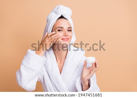 Portrait of charming cheery girl wear bathrobe applying night cream new good product isolated over beige pastel color background