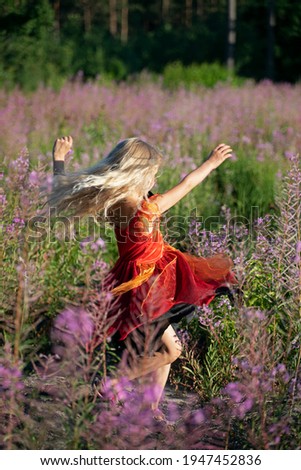 cute little blonde girl in an elegant fairy dress whirl in the flowers of fireweed forest. Festive mood, birthday during the global pandemic, Coronovirus.