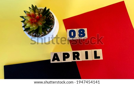 April 8 on wooden cubes.Next to it is a potted cactus on a multicolored red yellow black background.Calendar for April.