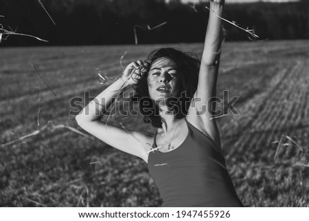 Portrait of a young beautiful brunette in a dress against the background of a mown wheat field, in the summer outdoors, sunset light. Woman happy dancing, black and white photo