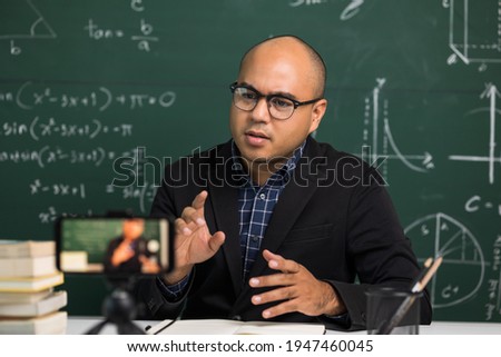 Indian young teacher man sitting teaching online video conference live stream by smartphone. Asian teacher teaching mathematics class webinar online for students learning.