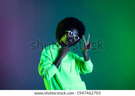 Photo of 80s lady clubbing show v-sign open mouth wear earphones glasses hoodie isolated gradient green neon background