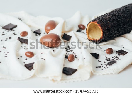 Traditional Hungarian kurtos kalacs known as chimney cake on a rustic tablecloth and chocolate Easter eggs. 
