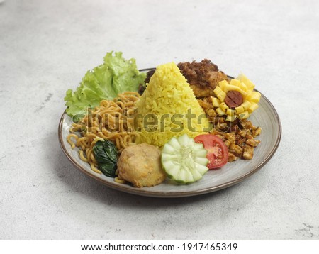 Tumpeng nasi kuning mini or Tumini, complete with all the side dishes such as chili fried potatoes, eggs, fried noodles, shredded chicken and perkedel Royalty-Free Stock Photo #1947465349