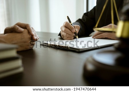 The lawyer is write drafting a legal document while listening to the client's information on the table with scale and gavel
