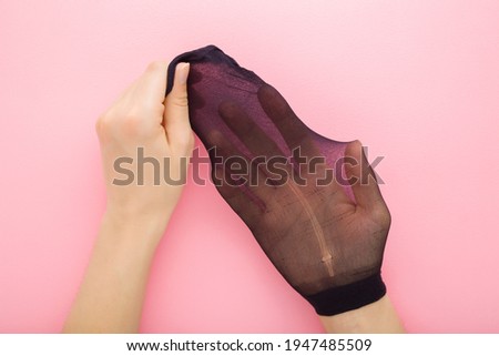 Young adult woman hands showing ripped short black nylon sock on light pink table background. Pastel color. Closeup. Point of view shot.