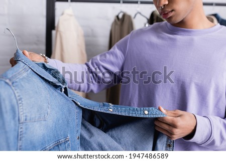 Cropped view of denim shirt in hand of african american showroom owner on blurred background