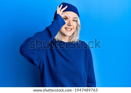 Young blonde girl wearing casual clothes smiling happy doing ok sign with hand on eye looking through fingers 