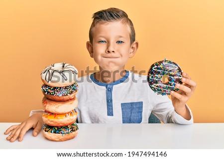 Adorable caucasian kid eating doughnuts for breakfast puffing cheeks with funny face. mouth inflated with air, catching air.  Royalty-Free Stock Photo #1947494146