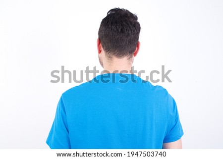 The back view of a young handsome caucasian man wearing blue t-shirt against white background. Studio Shoot.