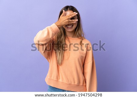 Young hispanic woman over isolated purple background covering eyes by hands and smiling