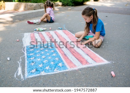 Two cute friends girls drawing American flag with colored chalks on the sidewalk near the house on sunny summer day. Kids painting outside. Creative development of children. Independence Day concept