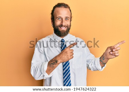Handsome man with beard and long hair wearing business clothes smiling and looking at the camera pointing with two hands and fingers to the side. 